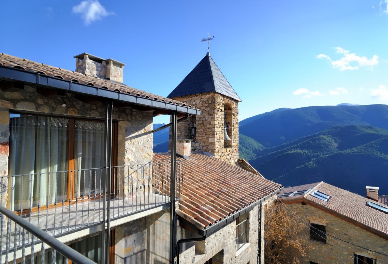 La casa de piedra con sus balcones y el campanario de Sant Climent